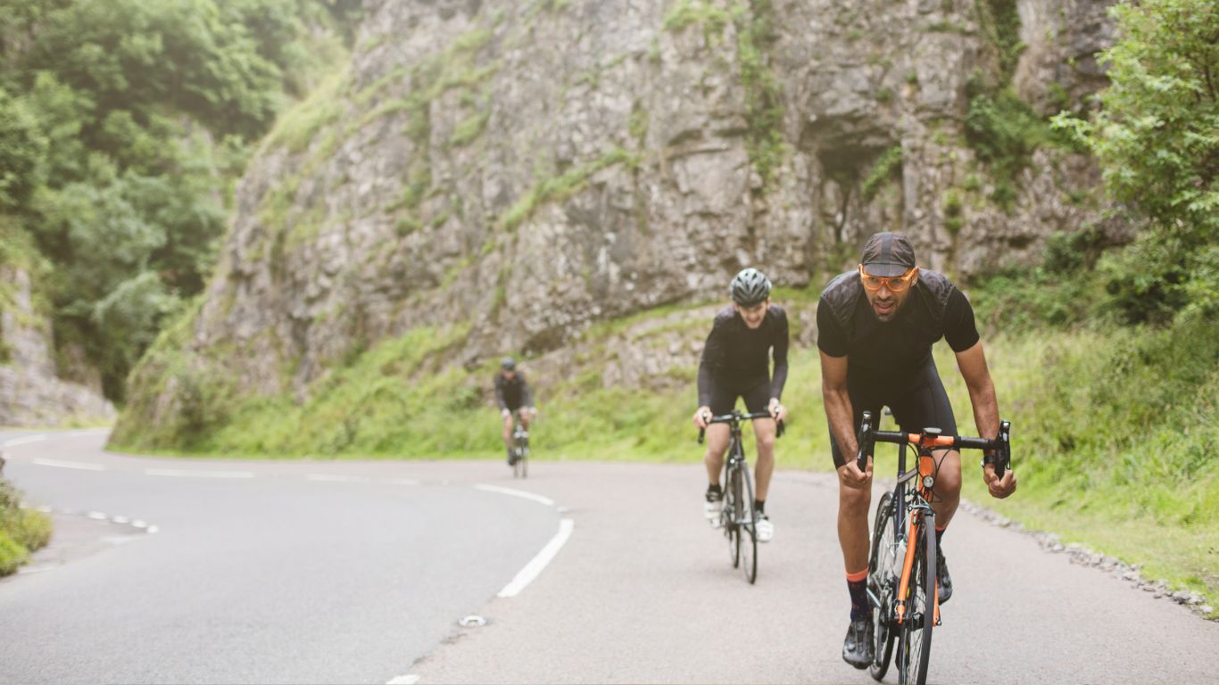 Three cyclists climbing uphill on a road through a gorge